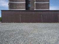 a building with a tower made of bricks is next to a park benches on gravel