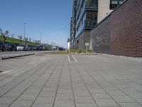 a brick and stone pavement with some grass next to buildings and cars in the background