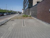 a brick and stone pavement with some grass next to buildings and cars in the background