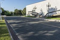 an empty street leading to a very big building with stairs on one wall and many windows and staircases on the second floor