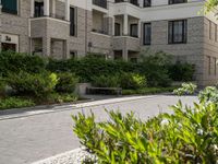 a bench is near an apartment building and bushes and trees in front of it outdoors