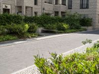 a bench is near an apartment building and bushes and trees in front of it outdoors