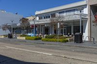 a large white building is on the side of the street near a busy intersection and tree - lined parking area