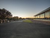 a sunset over a field near trees and benches at dusk next to a lake with cars