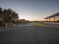 a sunset over a field near trees and benches at dusk next to a lake with cars