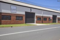 a row of cars driving down a street next to an industrial building with windows and three side doors