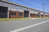 a row of cars driving down a street next to an industrial building with windows and three side doors