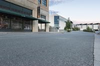 this is an empty street and the building in the back is a store front and a sidewalk with grass and rocks on each side