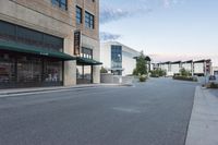 this is an empty street and the building in the back is a store front and a sidewalk with grass and rocks on each side