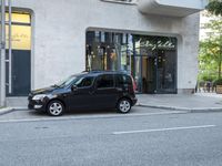 small car parked next to sidewalk in front of building with cafe window sign that reads ely