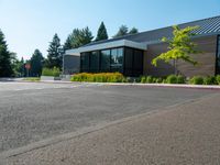 a building that has windows and plants in the front yard of it, in the middle of a gravel parking lot