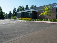 a building that has windows and plants in the front yard of it, in the middle of a gravel parking lot