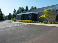 a building that has windows and plants in the front yard of it, in the middle of a gravel parking lot