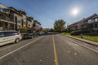 a street lined with cars in the middle of a residential area during the daytime, with the sun shining on the sky