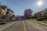 a street lined with cars in the middle of a residential area during the daytime, with the sun shining on the sky