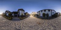 three houses on the side of the road with trees growing in front of it and sun setting on a street with sand and buildings