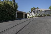 two street signs on each side of a road in front of a house with trees and palm