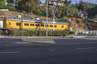 the yellow train is traveling along the railroad tracks in los angeles, california as seen from the corner of a small residential street