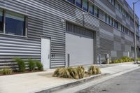 a building on the side of the street near a parking lot with plants growing in it