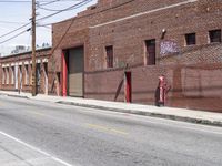 the red fire hydrant is next to a brick building on the corner of a city street