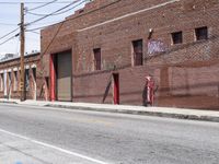 the red fire hydrant is next to a brick building on the corner of a city street