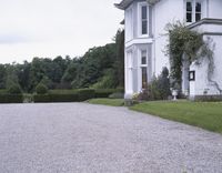 the view of a driveway that has a gravel path leading to the door and a large house behind