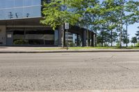 street view of large glass office building on corner street in urban area with green trees