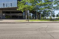 street view of large glass office building on corner street in urban area with green trees