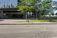 street view of large glass office building on corner street in urban area with green trees