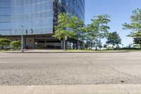 street view of large glass office building on corner street in urban area with green trees