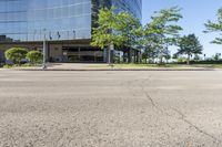 street view of large glass office building on corner street in urban area with green trees