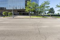 street view of large glass office building on corner street in urban area with green trees