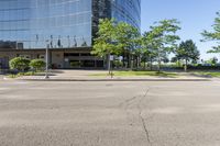 street view of large glass office building on corner street in urban area with green trees