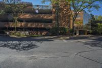 a parking garage is shown at an intersection in a city street corner with trees on either side and a large brick building in the background