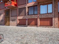 a brick paved area with red shutters and garage doors and windows, in a residential area