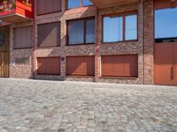 a brick paved area with red shutters and garage doors and windows, in a residential area