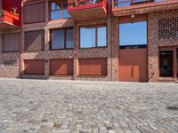 a brick paved area with red shutters and garage doors and windows, in a residential area