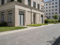 a block paved area with bushes in the front and sidewalk with brick paving and building behind