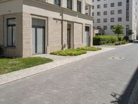 a block paved area with bushes in the front and sidewalk with brick paving and building behind