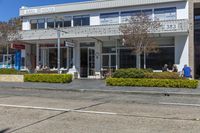 people sit at tables on the sidewalk in front of a large building with a store front