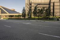 the paved street in front of an urban building is empty of cars, and a couple pedestrians have stopped on one side