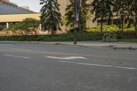 the paved street in front of an urban building is empty of cars, and a couple pedestrians have stopped on one side