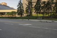 the paved street in front of an urban building is empty of cars, and a couple pedestrians have stopped on one side