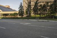 the paved street in front of an urban building is empty of cars, and a couple pedestrians have stopped on one side