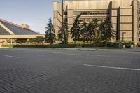 the paved street in front of an urban building is empty of cars, and a couple pedestrians have stopped on one side