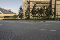 the paved street in front of an urban building is empty of cars, and a couple pedestrians have stopped on one side