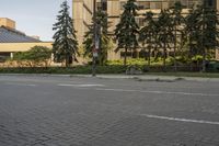 the paved street in front of an urban building is empty of cars, and a couple pedestrians have stopped on one side