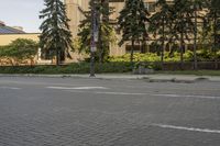 the paved street in front of an urban building is empty of cars, and a couple pedestrians have stopped on one side