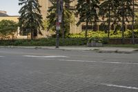 the paved street in front of an urban building is empty of cars, and a couple pedestrians have stopped on one side