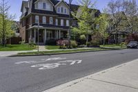 an empty street in front of a large house with bikes written on the sidewalk, in front of houses with trees